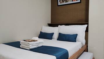 A neatly made bed with white and blue bedding, a stack of folded towels, and a framed picture on the wall.