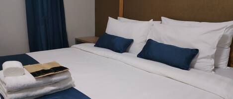 Una cama bien hecha con ropa de cama blanca y azul, un cabecero de madera y una mesita de noche con una lámpara.