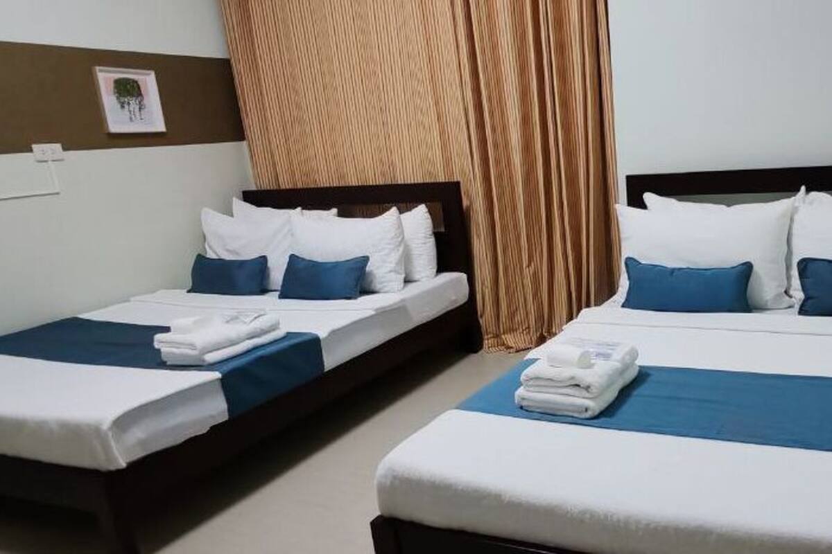 A hotel room with two single beds, a wooden nightstand, and a large window with curtains.