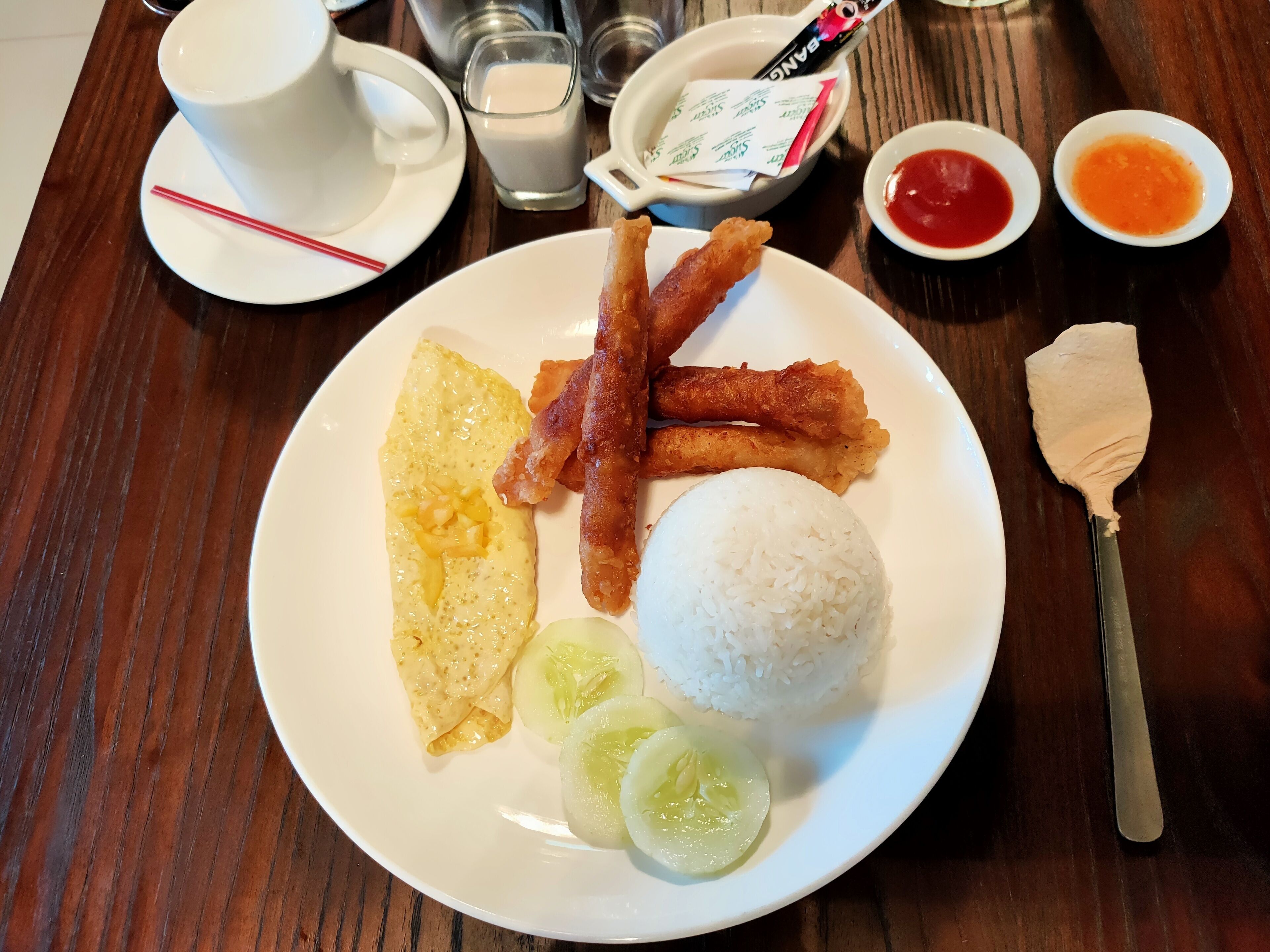Un plato con pescado frito, arroz, un huevo frito y rodajas de pepino.