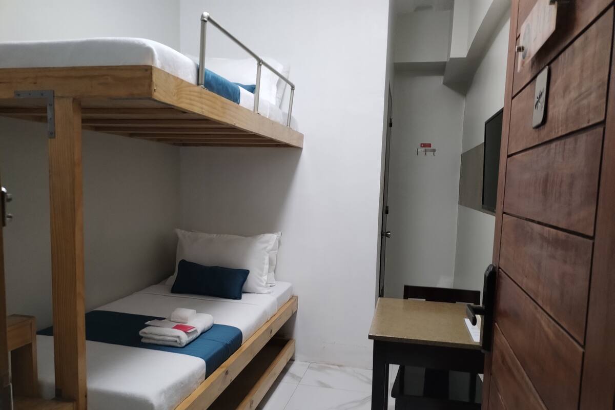 A bunk bed with a desk and a television in a small room.