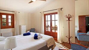 Habitación de hotel con una cama grande, una mesita de noche con lámpara, una silla, perchero y vistas al exterior a través de una puerta.