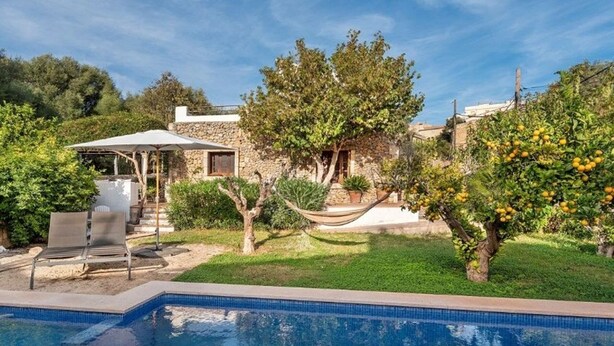 Zona junto a la piscina con una casa de piedra, una hamaca y un limonero.