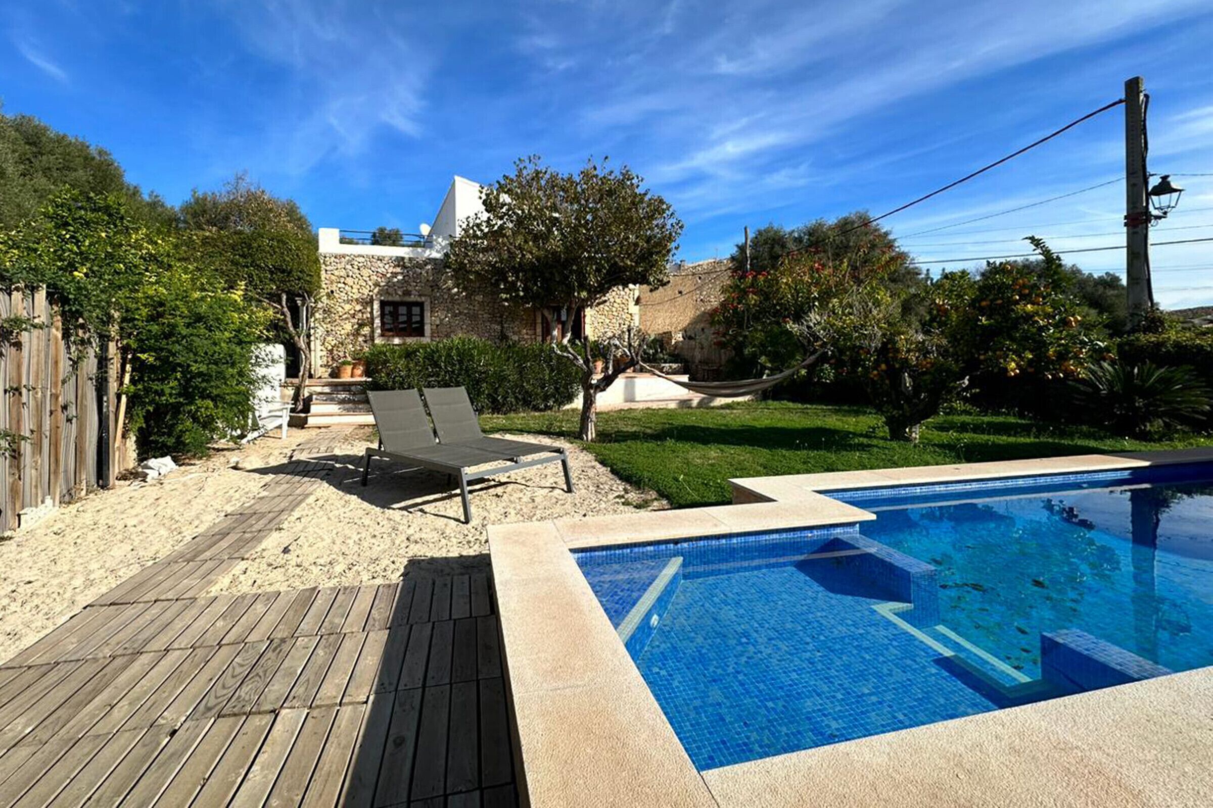 A backyard with a swimming pool, a wooden deck, and a stone house.