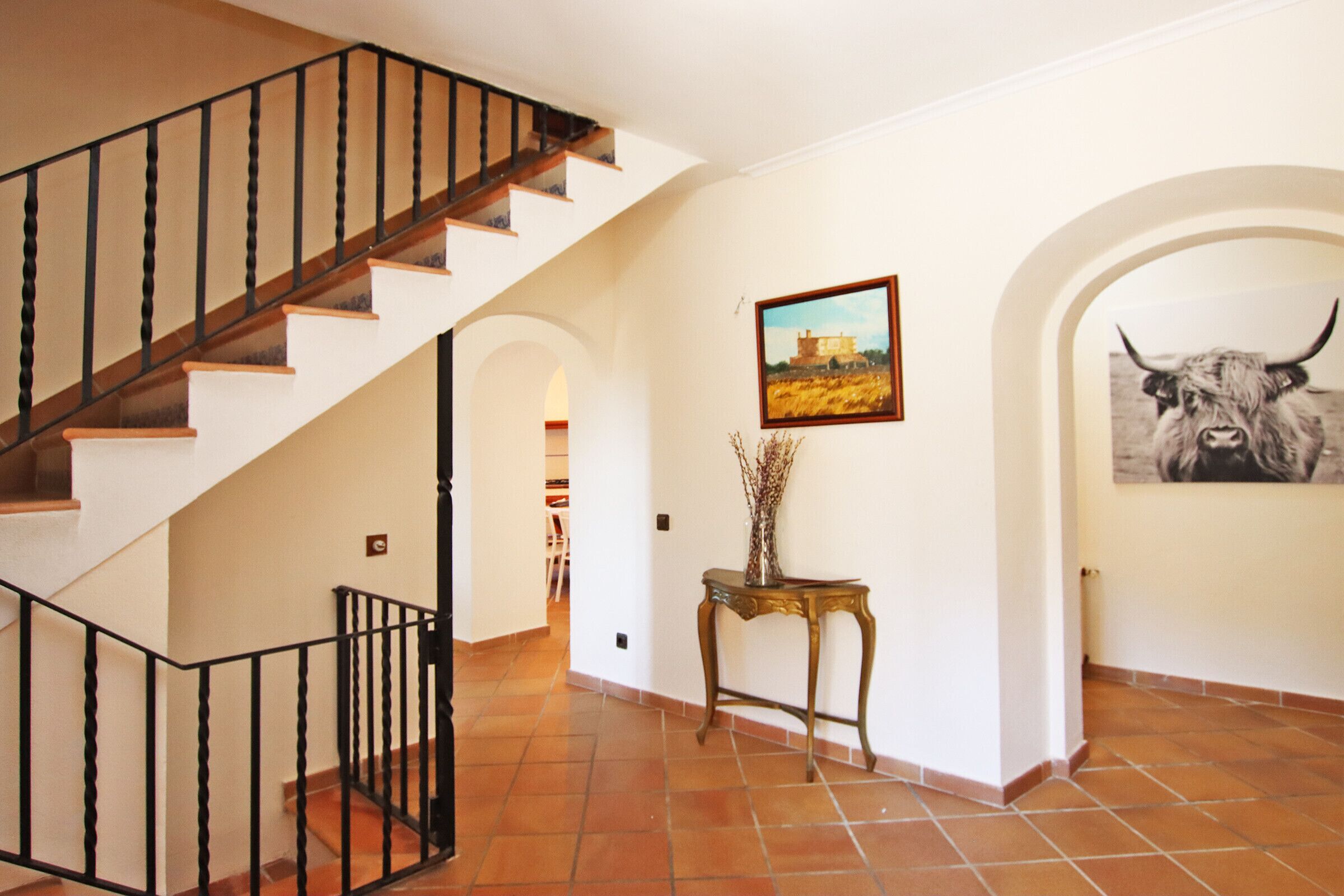 Un escalier avec des rampes noires, un tableau encadré accroché au mur et un vase décoratif posé sur une petite table.