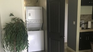 A laundry room with stacked washers and dryers, a potted plant, and a dark door leading to another room. - Peaceful Country Living (Nipawin)