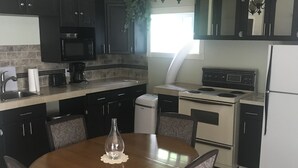 A kitchen with dark cabinets, a microwave, a stove, and a dining table with chairs. - Peaceful Country Living (Nipawin)