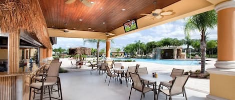 An outdoor seating area with tables and chairs, a pool, and a thatched roof structure.
