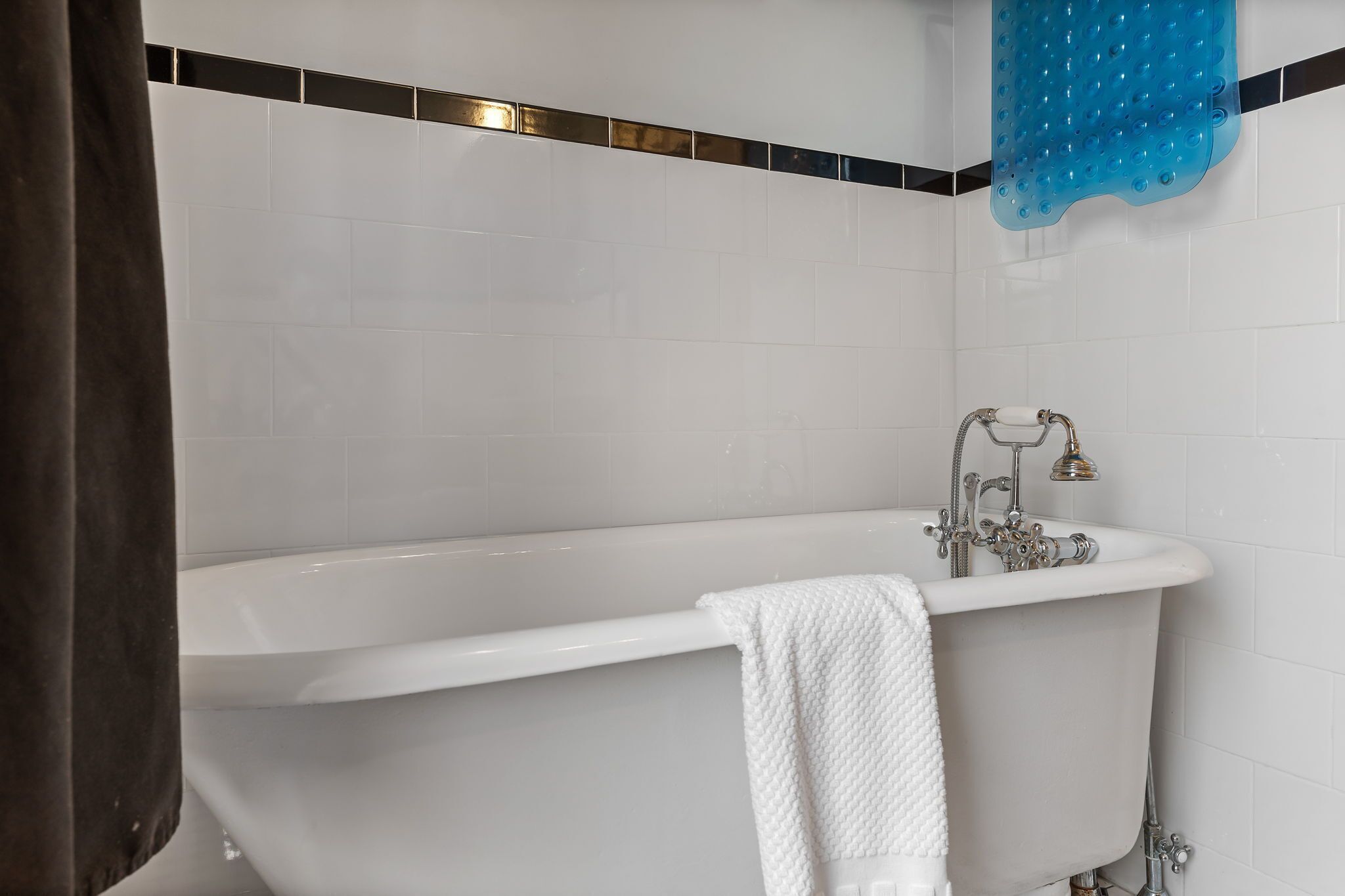 Un baño con una bañera blanca, una toalla blanca y un tapete de ducha azul.