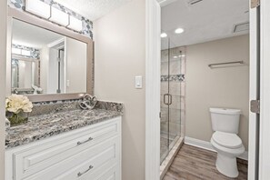 Un baño con encimera de mármol, inodoro blanco y cabina de ducha con mampara de vidrio.