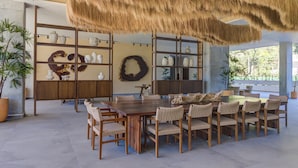 Ein großzügiger Essbereich mit einem großen Holztisch und Korbstühlen, umgeben von Regalen mit Dekoration und Pflanzen.
