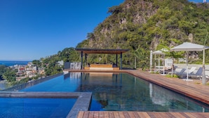 Ein Pool mit Holzterrasse, Liegestühlen und einem Pavillon mit Blick auf einen Hügel.