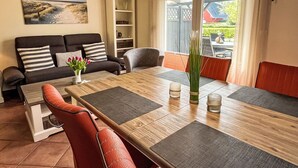Una sala moderna con una mesa de comedor de madera, sillas rojas, un sofá con cojines a rayas y una estantería.
