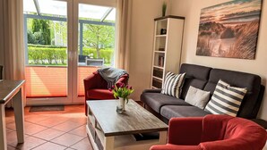 Una sala moderna con un sofá rojo, una mesa de centro con un florero y una estantería, además de un amplio ventanal con vistas a zonas verdes.