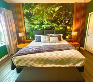 Ein Bett mit Kopfteil, zwei Nachttische und eine Wand mit einem tropischen Pflanzenwandbild.