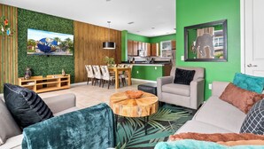Ein modernes Wohnzimmer mit grüner Akzentwand, einem Essbereich mit Holzmöbeln und einer Küche mit Holzausstattung.