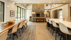 A modern kitchen with a stone fireplace, wooden beams, and a large dining area with bar stools. - Sable Rock Retreat- Modern Luxury w/ 5 beds, 6 ba, spa, sauna, 2nd living room. (Bend)