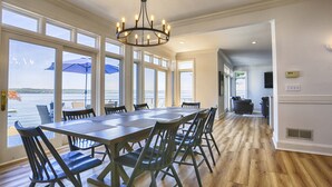 A spacious dining area with a large table and chairs, large windows offering a view of the water, and a chandelier. - Lakeview Heaven - Elegant Canandaigua Lake Getaway | Dock + Hot Tub (Canandaigua)