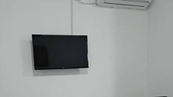 A bedroom with a bed, a TV mounted on the wall, a dresser, and an air conditioning unit.