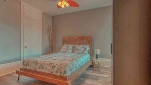 A bedroom with a wooden bed, a nightstand, a lamp, and a ceiling fan. - Historic Riverfront Tropical Gem w/ River Views (Harrisburg)