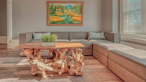 A modern living room with a wooden coffee table, a gray sofa with cushions, and a painting of a landscape on the wall. - Historic Riverfront Tropical Gem w/ River Views (Harrisburg)