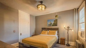 Une chambre à coucher avec un lit, une table de chevet, une lampe sur pied, un radiateur et un tableau accroché au mur.