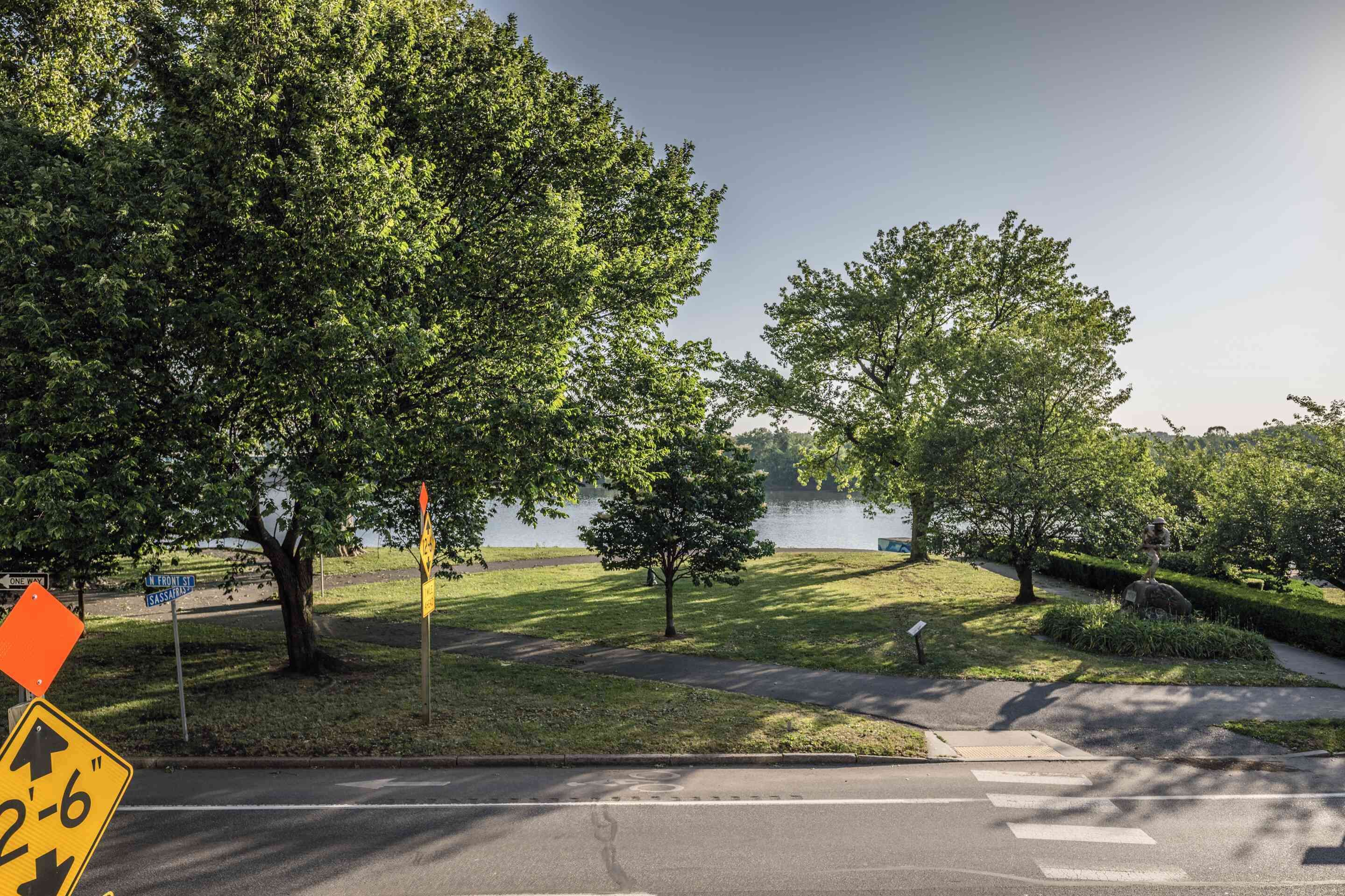 A road with a 2-6' sign, trees, a grassy area, and a body of water in the background.