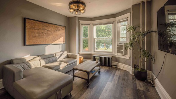 Un salon moderne avec un canapé d’angle, une table basse, une carte accrochée au mur et une grande fenêtre donnant sur un paysage verdoyant.