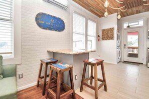 Une pièce avec un mur en briques blanches, une enseigne bleue, des tabourets en bois, un canapé vert et un plafond en bois.
