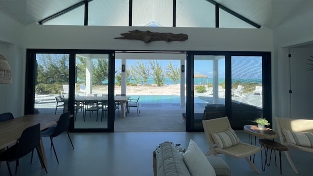 Un vaste espace de vie avec une grande porte-fenêtre coulissante donnant sur une piscine, un plafond haut agrémenté de fenêtres de toit et une vue sur la plage.