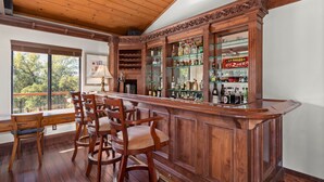 Un espace bar avec des tabourets de bar en bois, un comptoir en bois et des étagères remplies de bouteilles.