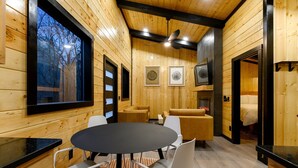 L’intérieur d’un chalet en bois, avec une table ronde, des chaises blanches, un ventilateur de plafond et des œuvres d’art encadrées accrochées aux murs.