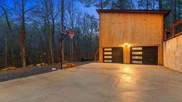 A modern wooden cabin with a concrete driveway and a basketball hoop.