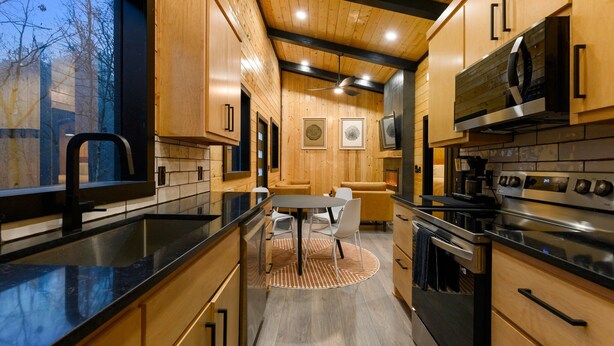 Une cuisine moderne avec des meubles en bois, un plan de travail noir, un coin repas avec une table ronde et des chaises, et une grande cuisinière.
