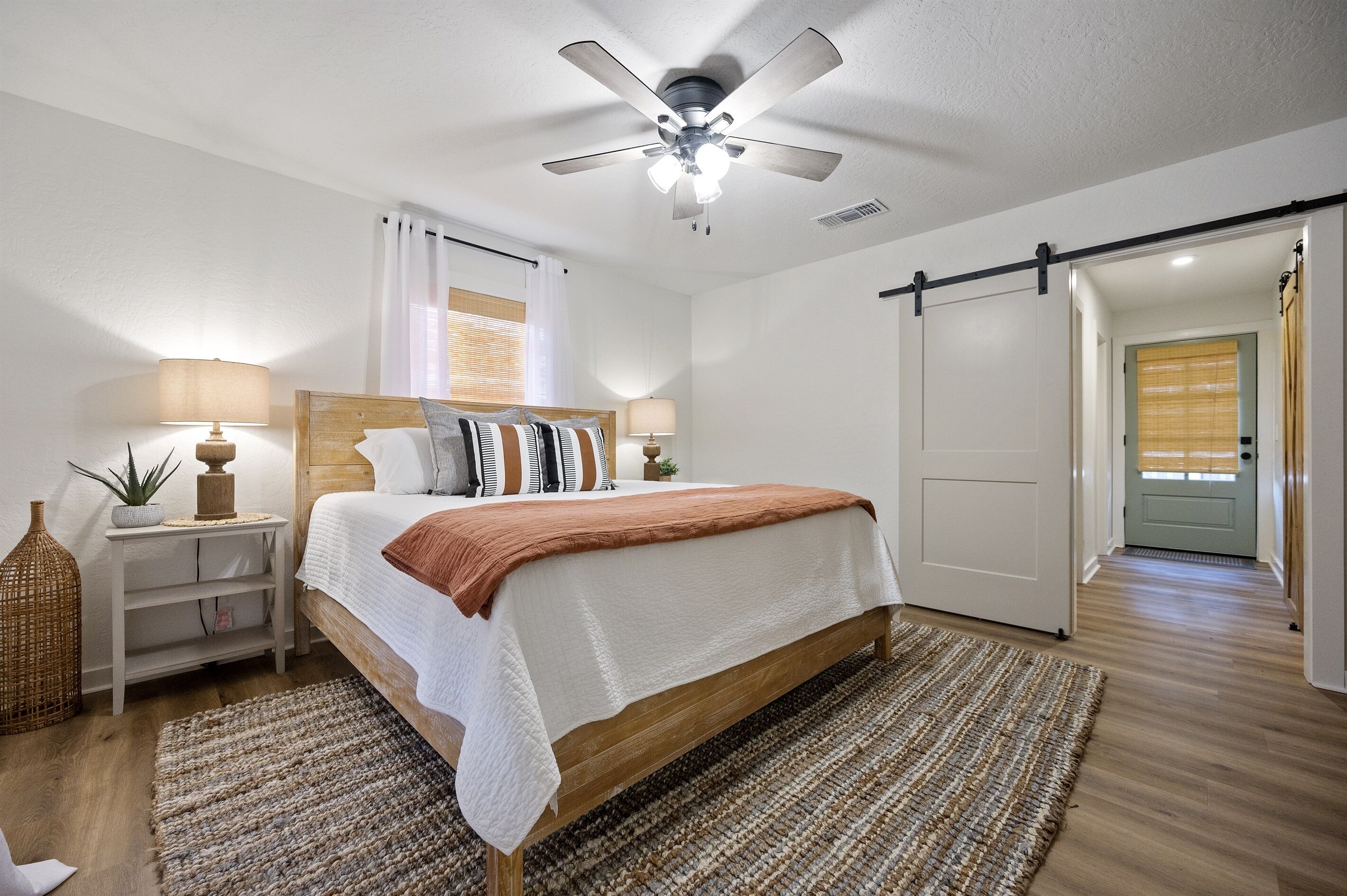 Une chambre à coucher comprenant un lit, des tables de chevet, un ventilateur de plafond et une porte coulissante.