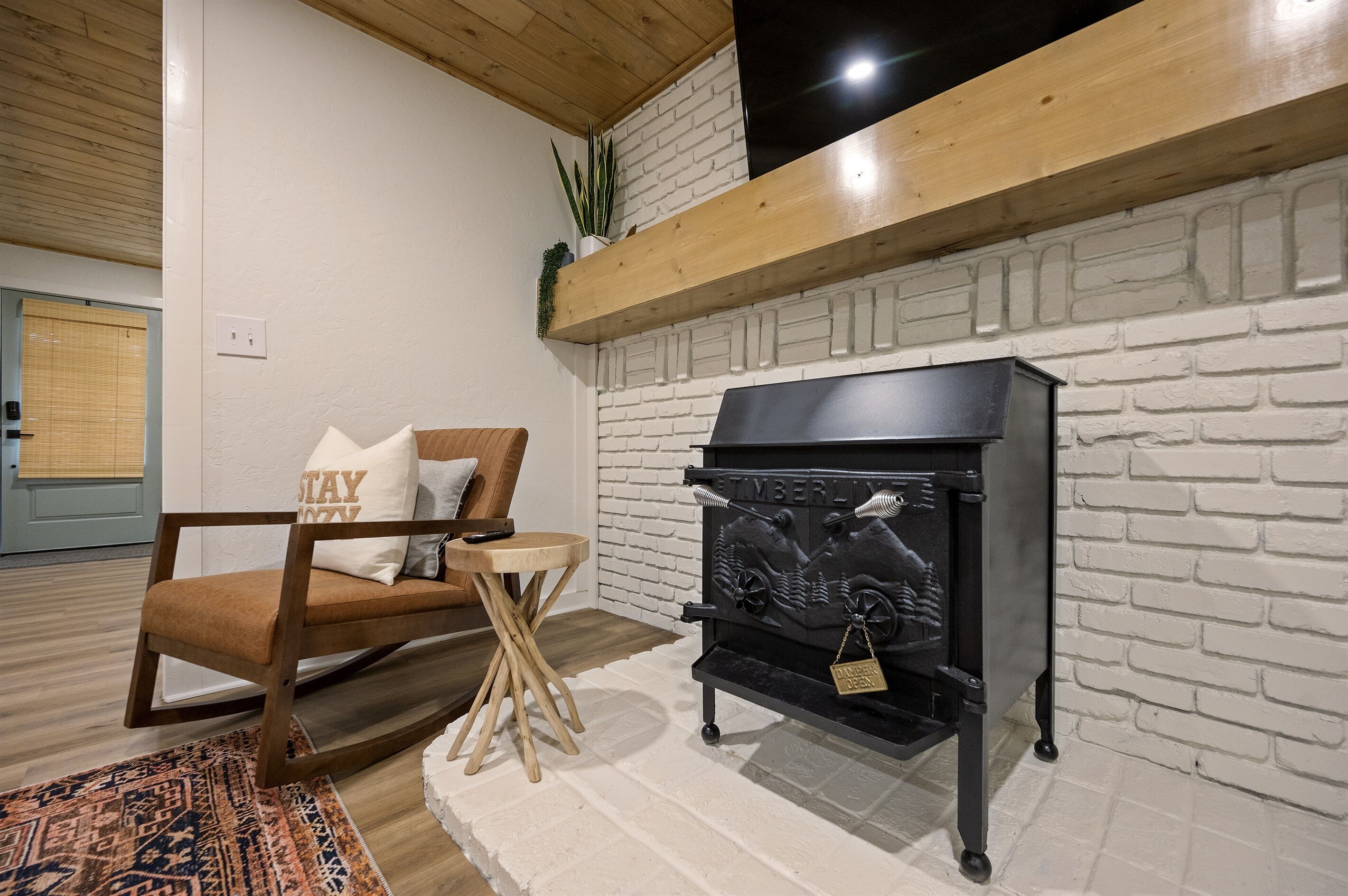Un salon chaleureux avec un fauteuil à bascule en bois, une petite table ronde et une cheminée noire portant l’inscription « Timberline ».