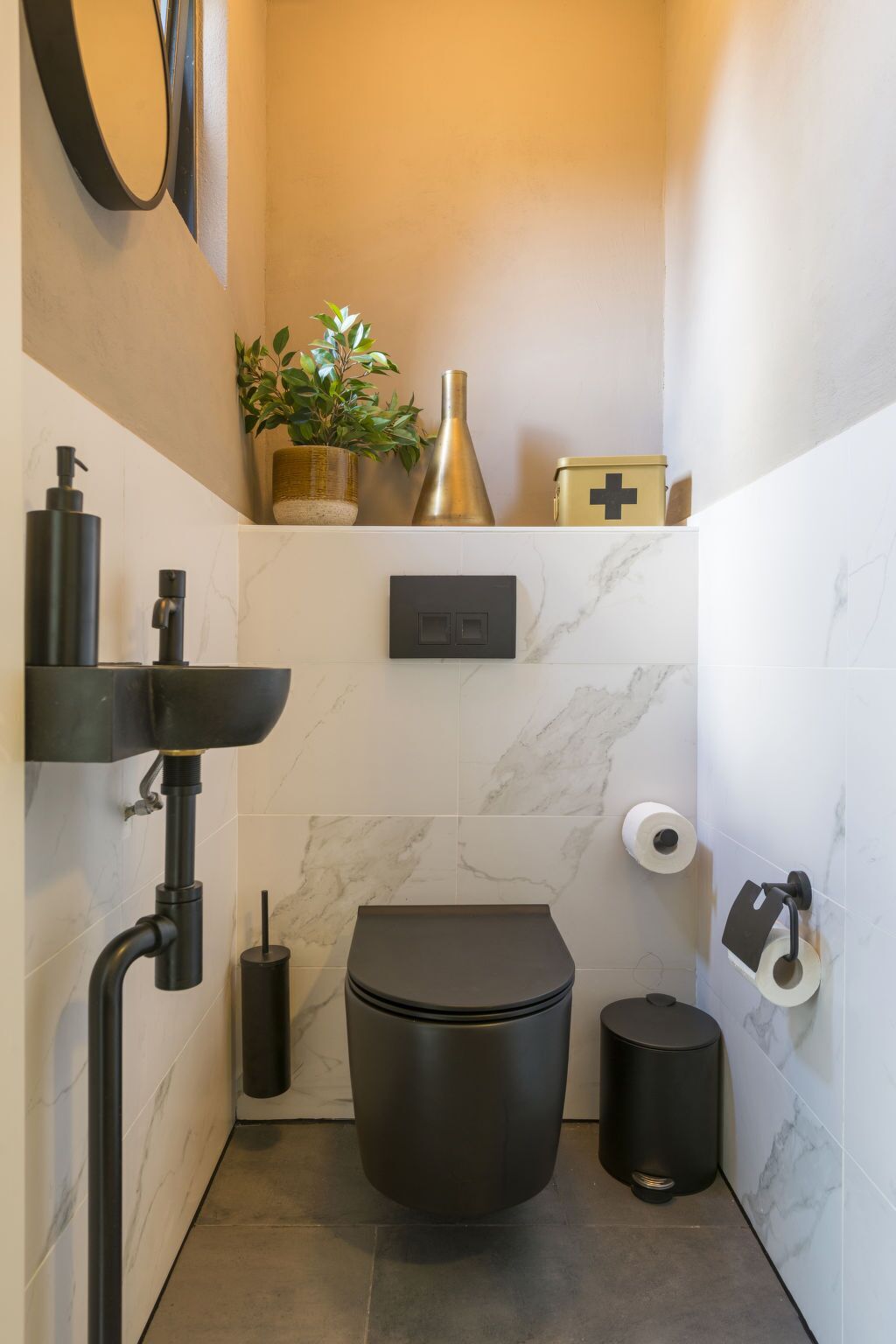 Un bagno moderno con servizi igienici, bidet, lavandino e un piccolo ripiano con una pianta e oggetti decorativi.