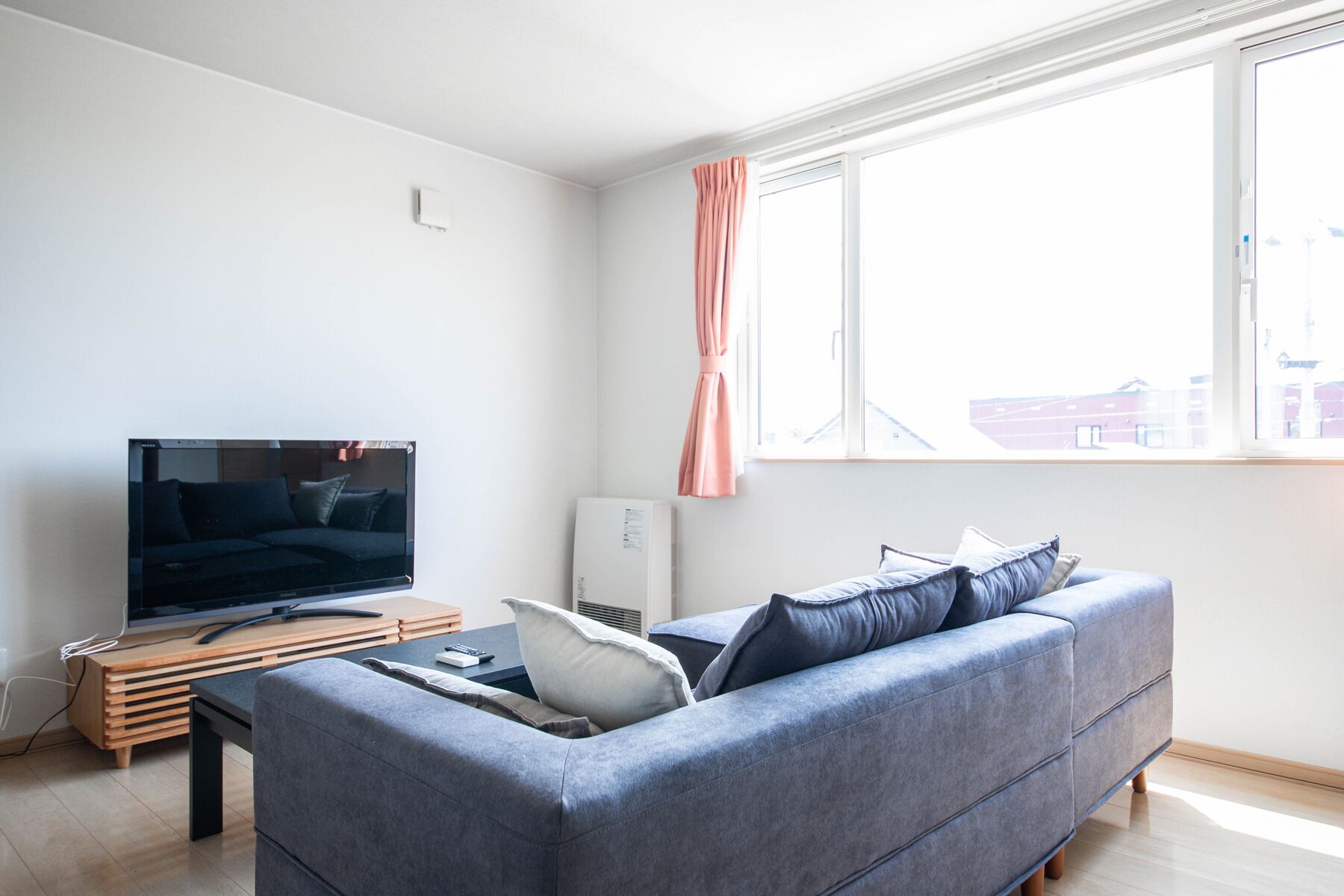 Ein modernes Wohnzimmer mit einem grauen Sofa, einem Flachbildfernseher und einem Fenster mit einem rosa Vorhang.