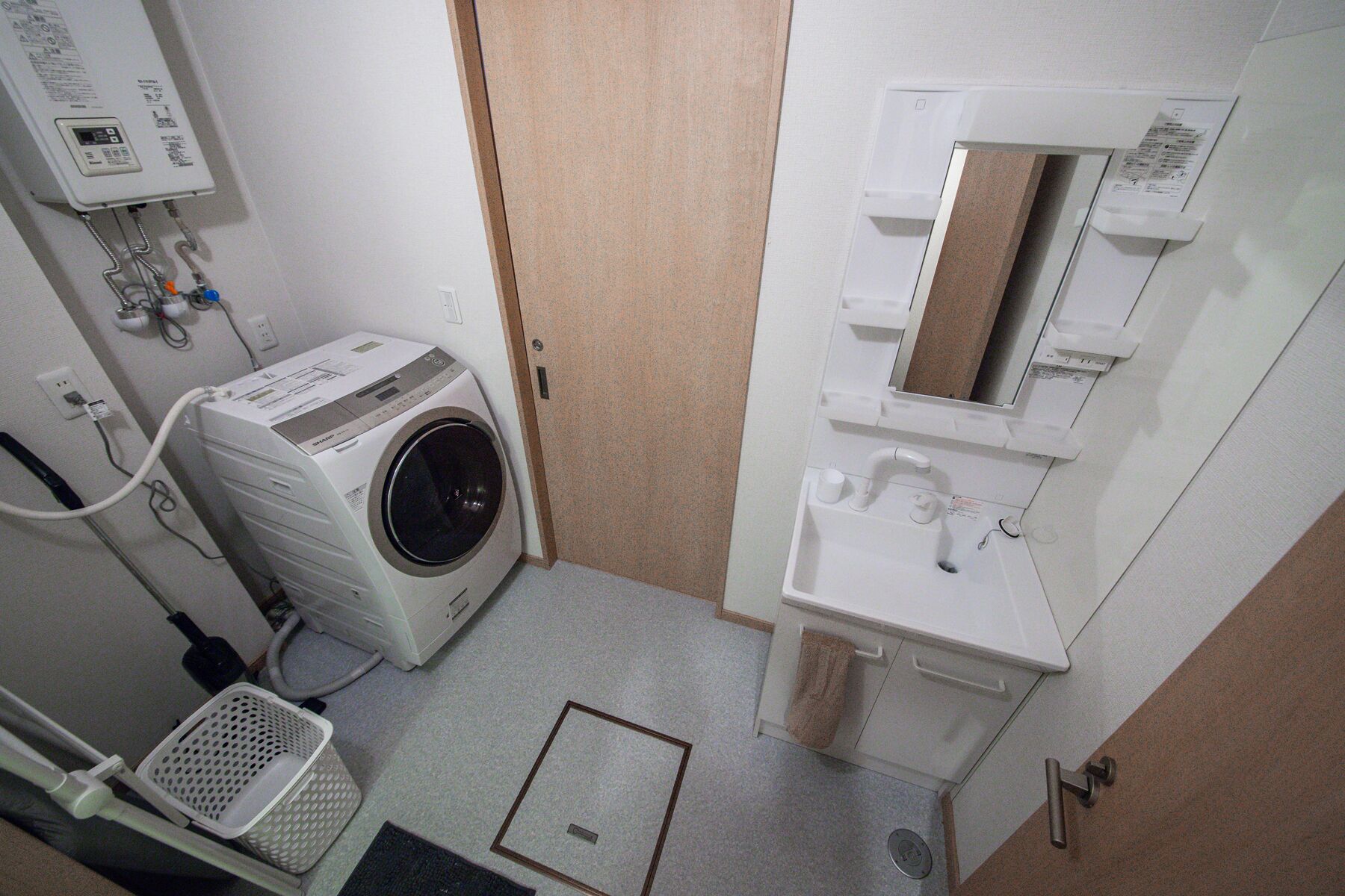 A laundry room with a front-loading washing machine, a sink, and a mirror.