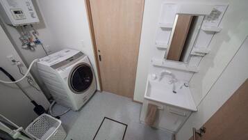 A laundry room with a front-loading washing machine, a sink, and a mirror.