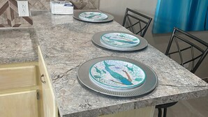 Uma cozinha com bancada de mármore, dois pratos com design de pássaros, uma cadeira marrom e uma parede com padrão geométrico.
