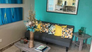 Uma sala de estar com parede verde-água, um sofá com almofadas estampadas, uma mesa de centro com livros e um vaso decorativo.