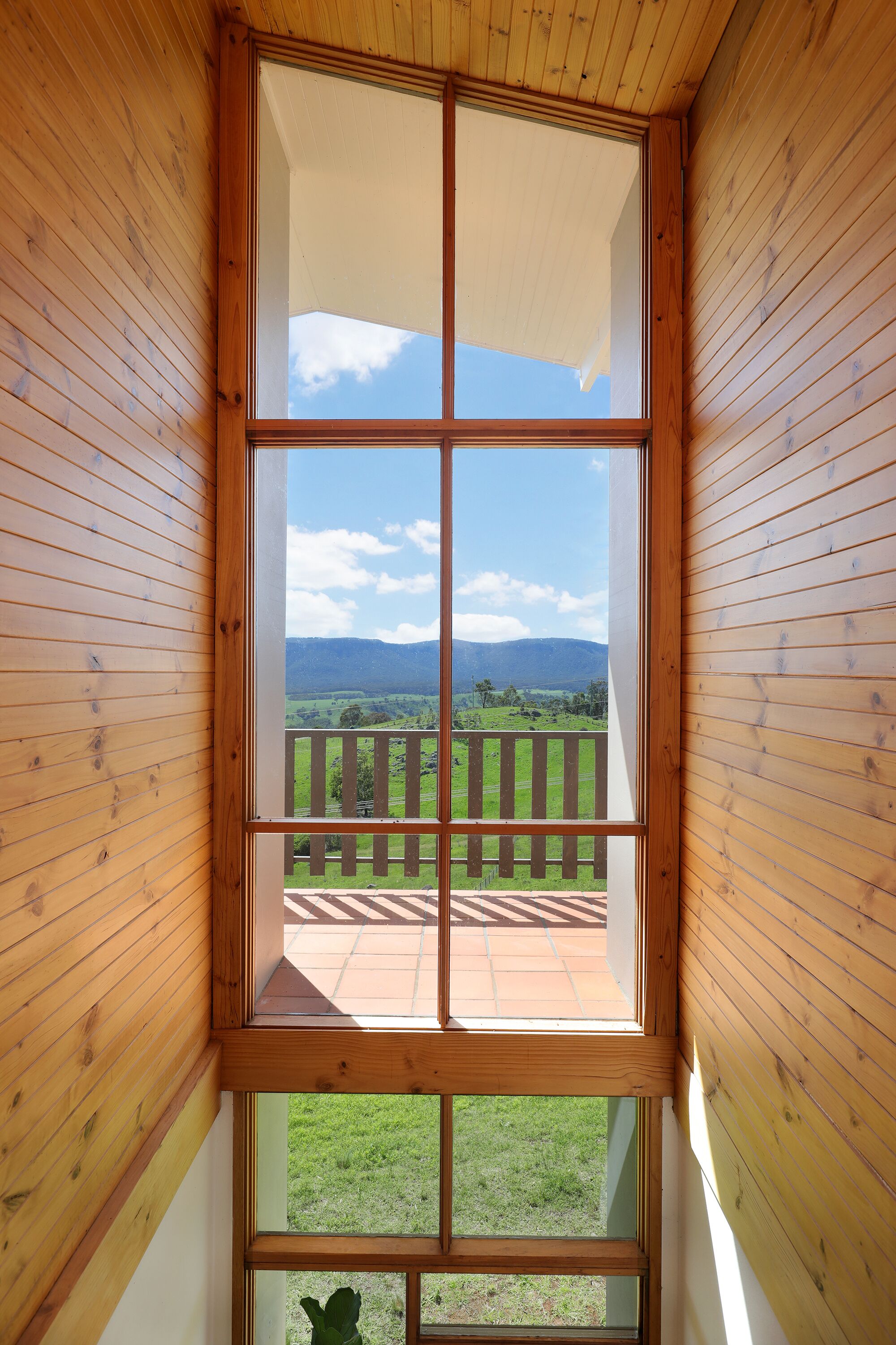 A wooden-framed window with a view of a grassy landscape and mountains.