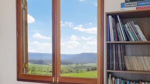 Une pièce dotée d’une grande fenêtre donnant sur un paysage verdoyant, d’une bibliothèque remplie de livres et d’un canapé rose agrémenté de coussins.