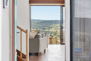 A modern interior with a sofa and a small table, a glass door leading to a balcony with a view of a hilly landscape.
