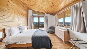 A bedroom with a wooden ceiling, a bed, a desk, and a view of the outdoors.