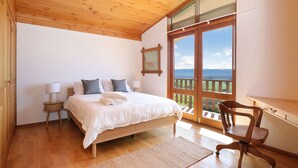 Une chambre avec un lit en bois, des lampes de chevet, un bureau et une vue sur l’extérieur.