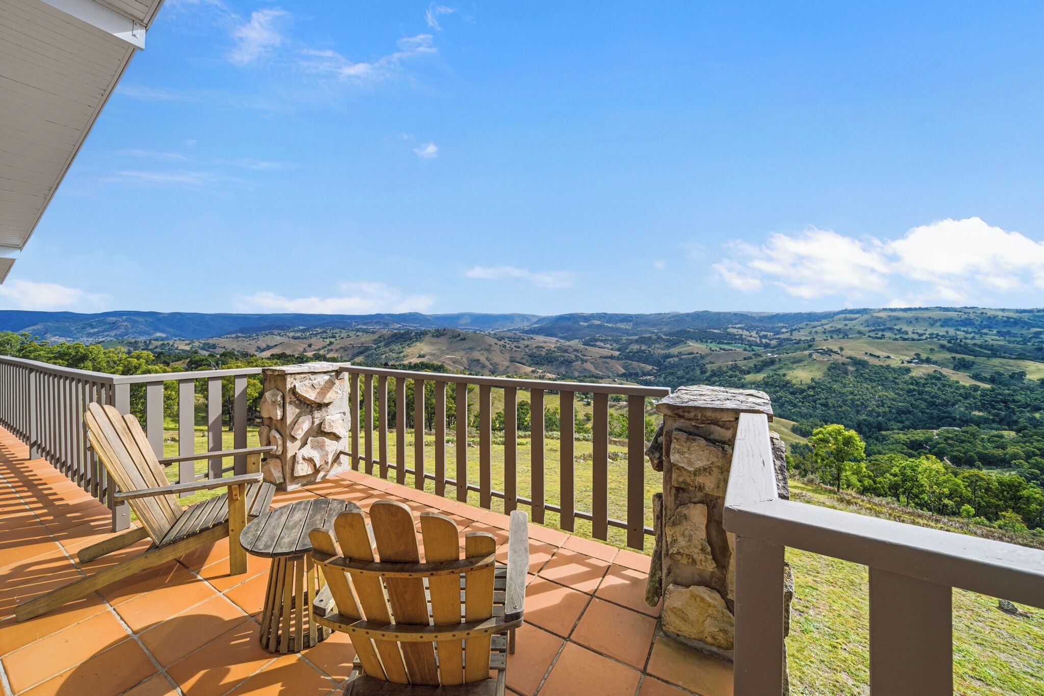 A terrace with a view of rolling hills, wooden chairs, and a stone pillar.