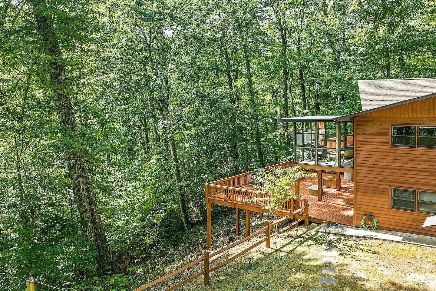 A wooden cabin with a deck and a glass enclosure, surrounded by dense forest.