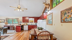 A kitchen with wooden cabinets, a dining table with chairs, a ceiling fan, and a mounted deer head.